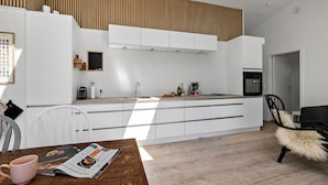 Een moderne keuken met witte kasten, een houten plafond en een eethoek met een houten tafel en een tijdschrift.