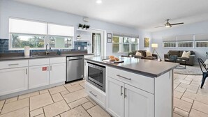 Une cuisine moderne avec des meubles blancs, un îlot central et un coin repas comprenant un canapé et une table basse.