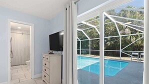 Une salle de bain avec douche, un meuble-lavabo équipé d’un téléviseur et une grande fenêtre donnant sur une piscine.