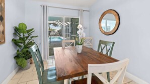 Un coin repas avec une table en bois et des chaises blanches, une plante en pot et un miroir rond accroché au mur.