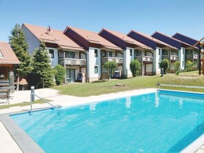 A swimming pool with a clear blue water, surrounded by a building with balconies and a covered patio area.