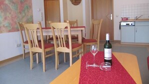 Un coin repas avec une table dressée pour deux personnes, des chaises en bois, une nappe rouge et une bouteille de vin.
