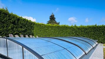 Ein modernes Bauwerk mit einer gewölbten Glasdachkonstruktion, umgeben von einer ordentlich geschnittenen Hecke und blauem Himmel.