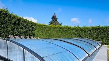 A modern architectural structure with a curved glass roof, surrounded by a neatly trimmed hedge and a clear blue sky.