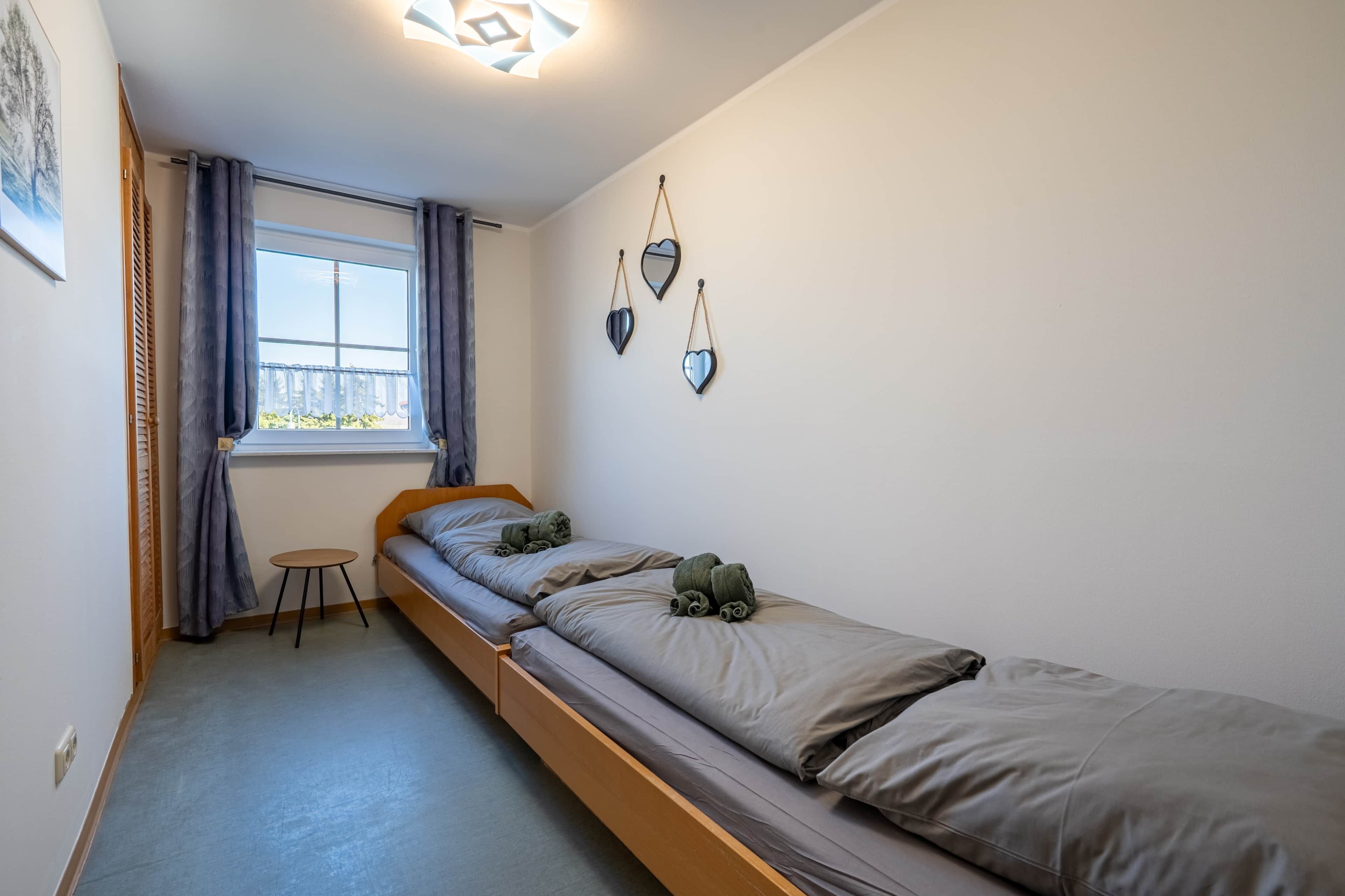 A single bed with a wooden frame, a small table, and a window with curtains.