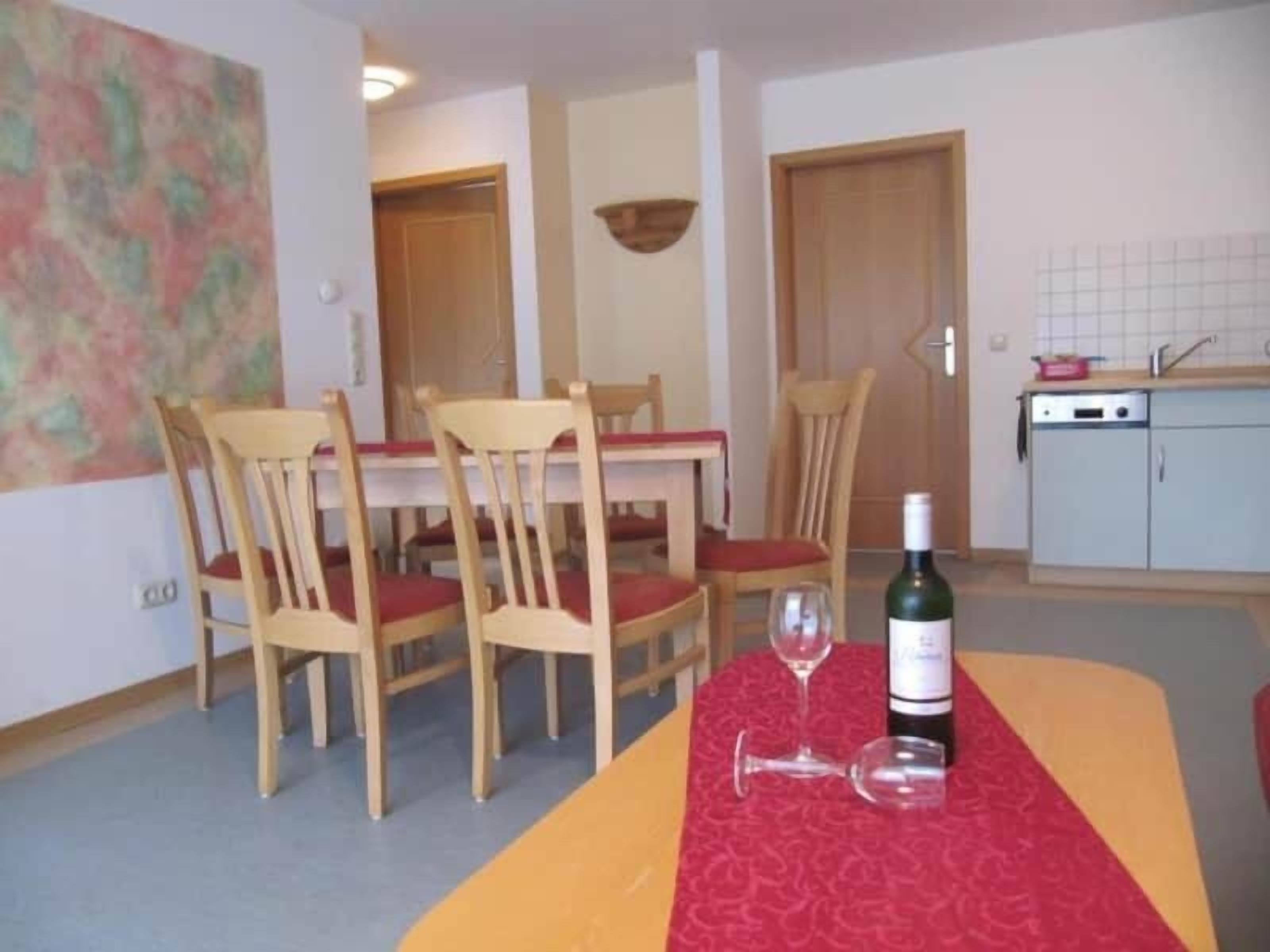 Un comedor con sillas de madera y una mesa, una botella de vino y copas sobre la mesa.