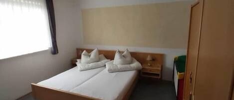 A single-bed room with a wooden headboard, a bedside table with a lamp, and a wardrobe.