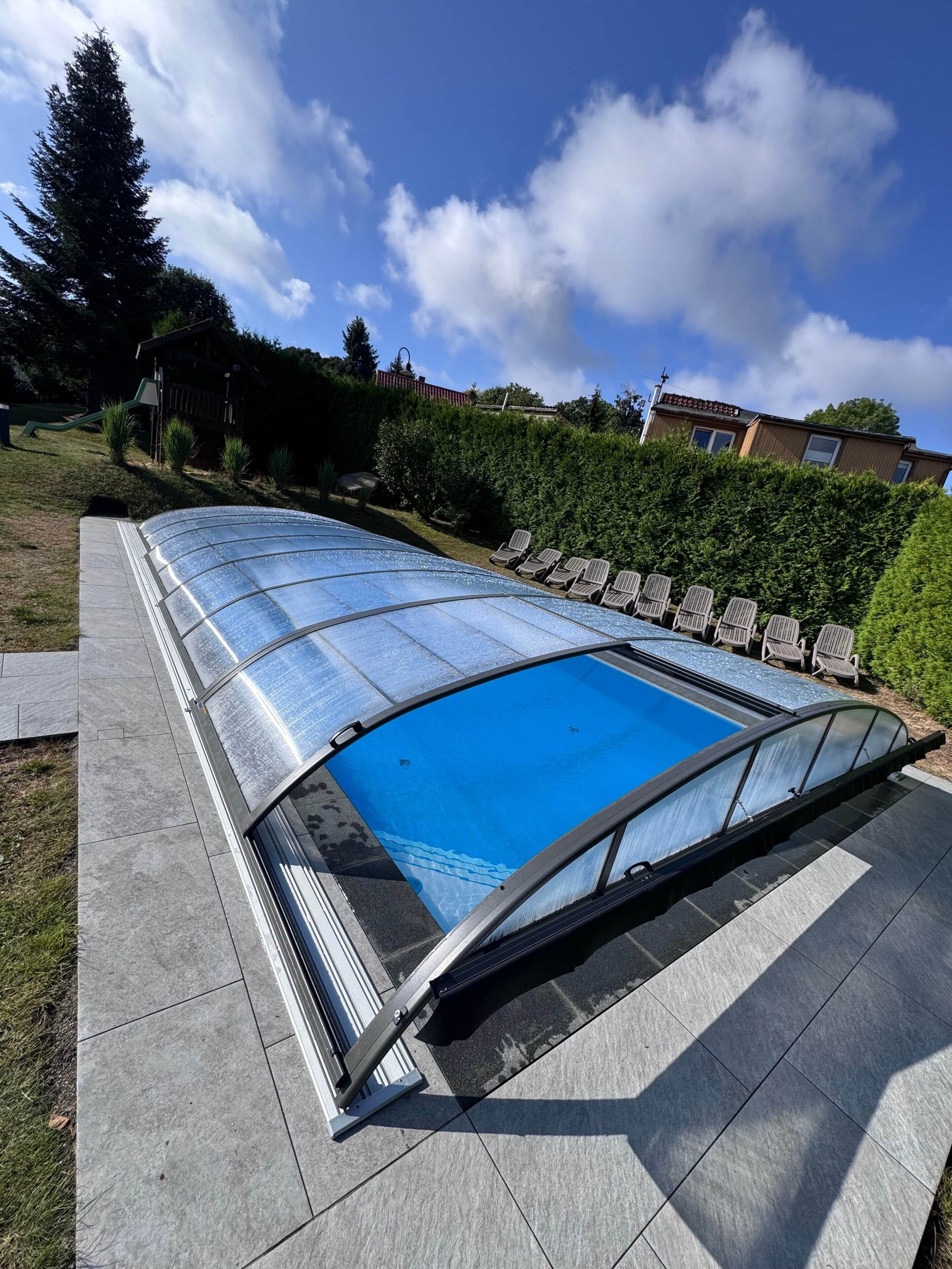 Ein Pool mit Glasabdeckung, umgeben von einer Terrasse mit Stühlen.