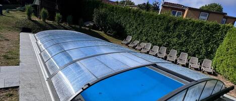 A swimming pool with a glass enclosure, surrounded by a patio area with chairs.