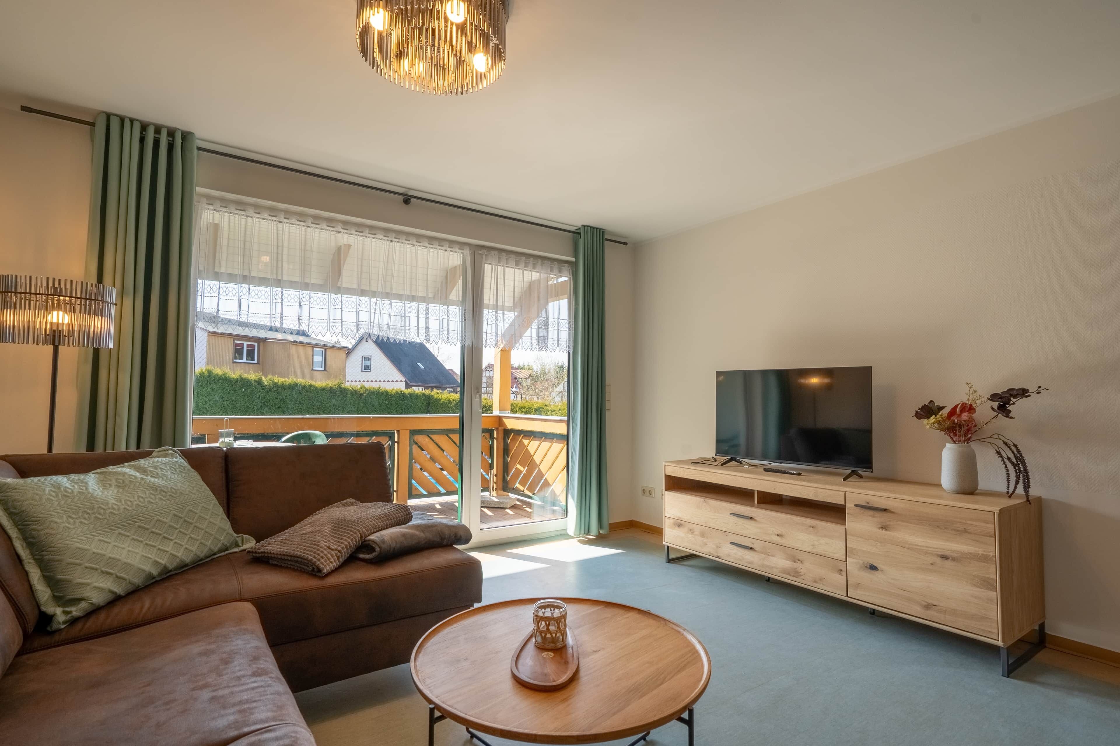 A modern living room with a sofa, TV, wooden cabinet, and a balcony with a view.