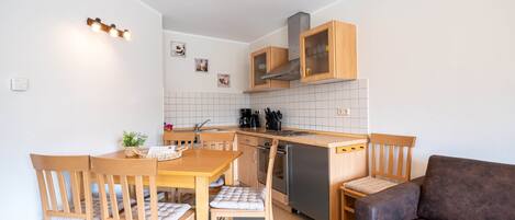 A compact kitchen with wooden cabinets, a dining table with chairs, a sofa, and a small countertop.
