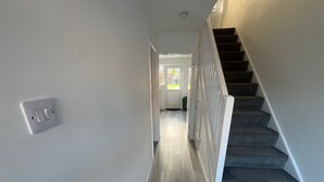 Un couloir avec un escalier sur la droite, un interrupteur sur la gauche et une porte au fond.