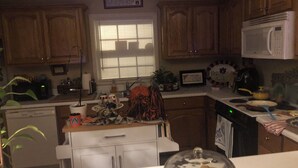 A kitchen with wooden cabinets, a microwave, and a stove. There is a window with blinds, a plant, and various kitchen items on the counter. - Charming 2-bedroom townhome in welcoming Auburn with AC, WiFi, 1897 Sqare feet (Auburn)
