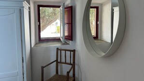 A room with a wooden chair, a small window with red shutters, and a round mirror on the wall. - Herdade da Yucca (Alandroal)