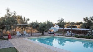 A rectangular swimming pool with a pergola and lounge chairs in a landscaped backyard. - Herdade da Yucca (Alandroal)
