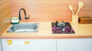 A kitchen with a sink, faucet, and a gas stove. There are wooden spoons in a holder and a dish soap dispenser. - Dieng Luxury Camp By Travelink (Kejajar)