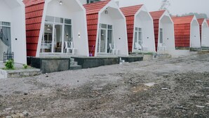 A row of white buildings with red roofs, each with a small porch and white chairs. - Dieng Luxury Camp By Travelink (Kejajar)