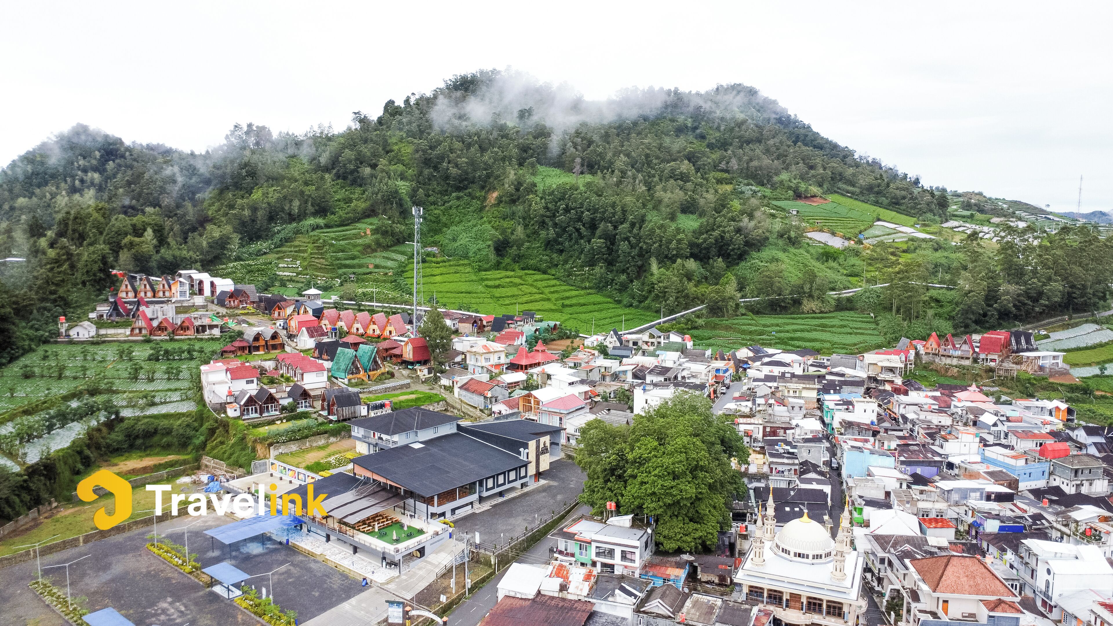 A town with a mix of traditional and modern buildings, a mosque, and terraced fields.