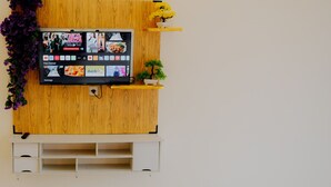 A wall-mounted TV with a wooden panel and a shelf with a potted plant. - Dieng Luxury Camp By Travelink (Kejajar)
