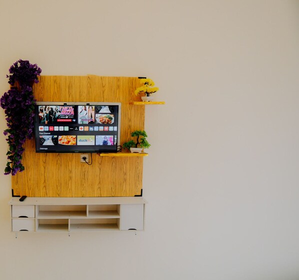 A wall-mounted TV with a wooden panel and a shelf with a potted plant. - Dieng Luxury Camp By Travelink (Kejajar)