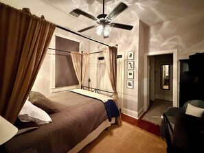 A bedroom with a four-poster bed, a ceiling fan, and a view of the hallway.