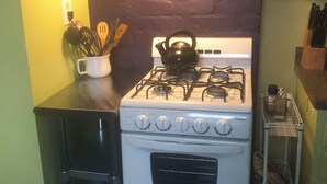 A compact kitchen with a white stove, a black kettle, and a utensil holder on the counter. - Cozy, Humble 1-Bedroom Near Ferry - Great for Travel Nurses! (New Orleans)