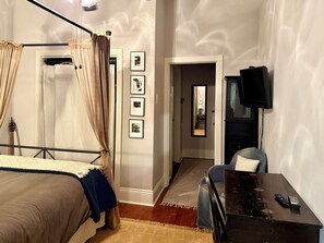 Une chambre à coucher avec un lit à baldaquin, une télévision, un bureau avec une télécommande et des tableaux encadrés accrochés au mur.