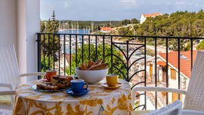 A balcony with a table set for breakfast, overlooking a marina and coastal town. - Charming 4-BR Villa with Heated Pool and Sea Views, Close to Beach (Milna)