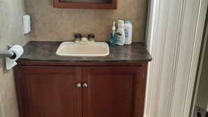 A bathroom with a wooden vanity, a mirror, and toiletries on the countertop.