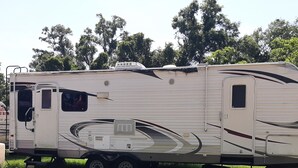 A white RV with a covered living area, a small enclosed kitchen, and a slide-out shower.