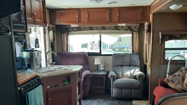 An RV interior with a kitchenette, seating area, and a window with a view.