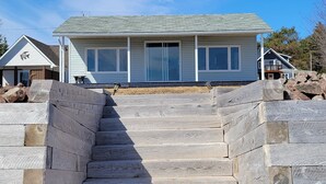 A staircase leading to a house with a gabled roof and large windows. - Oceanfront cottage with private beach access near Shediac, New Brunswick (Grande-Digue)