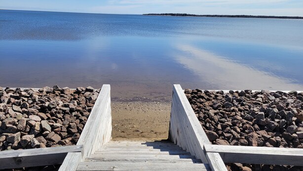 A wooden staircase leading to a sandy beach with a rocky shoreline. - Oceanfront cottage with private beach access near Shediac, New Brunswick (Grande-Digue)