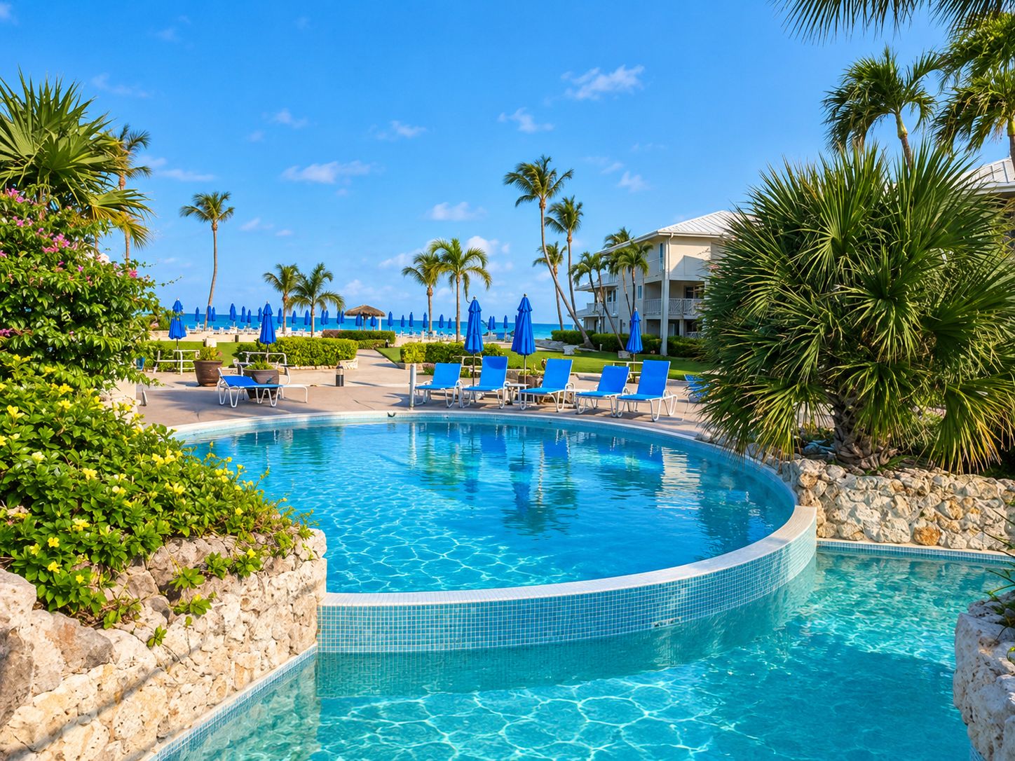 A pool area with lounge chairs and umbrellas, surrounded by palm trees and a building in the background.
