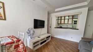 A living room with a flat-screen TV mounted on the wall, a standing fan, and a window with a view of the outside. - SUH Copacabana 105 Metro Posto 5 (Rio de Janeiro)