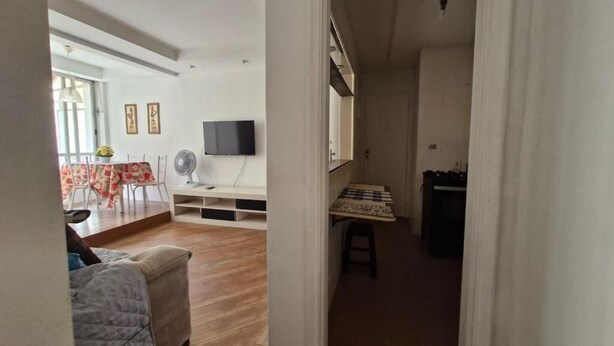 A living room with a sofa, a dining area with a table and chairs, a TV mounted on the wall, and a small table with a fan. - SUH Copacabana 105 Metro Posto 5 (Rio de Janeiro)