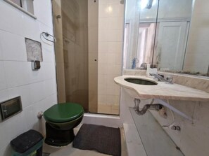 Une salle de bain avec des toilettes vertes, un lavabo avec un miroir et un espace douche.