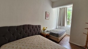 A bedroom with a large bed, a smaller bed, a nightstand with a vase of flowers, a picture on the wall, and a window with curtains. - SUH Copacabana 105 Metro Posto 5 (Rio de Janeiro)