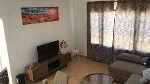 Un soggiorno con televisione a schermo piatto, un divano, un tavolino e un quadro appeso al muro.