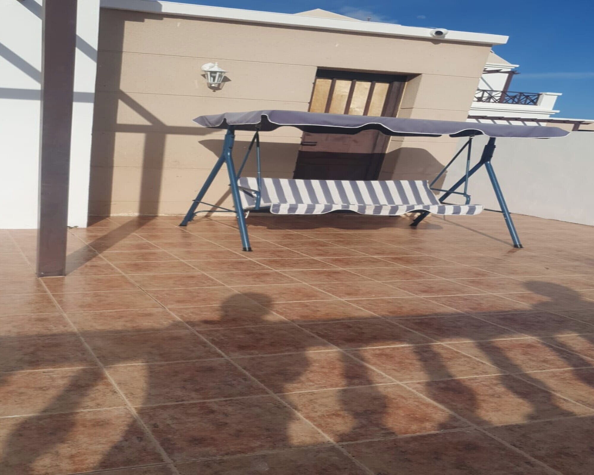 A patio area with a striped outdoor table and chairs, a tiled floor, and a building with a balcony in the background.