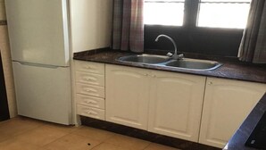 Una cucina con frigorifero, lavello, pensili e una finestra con tende.