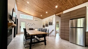 A modern kitchen with a wooden ceiling, a large stainless steel refrigerator, and a dining area with a wooden table and chairs.
