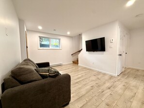 A modern living room with a sofa, a flat-screen TV mounted on the wall, and a staircase leading to an upper level. - Zénitude En Forêt Chalet – Spa & Precious Moments (Saint-Damien-de-Buckland)