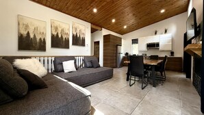 A modern living area with a sofa, dining table, and kitchen area. - Zénitude En Forêt Chalet – Spa & Precious Moments (Saint-Damien-de-Buckland)