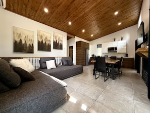 A modern living area with a sofa, dining table, and kitchen area. - Zénitude En Forêt Chalet – Spa & Precious Moments (Saint-Damien-de-Buckland)