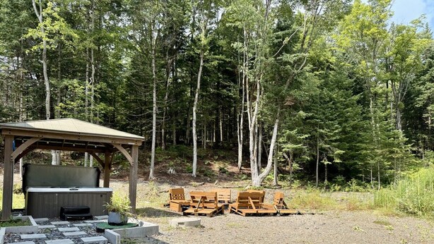 A covered outdoor seating area with a hot tub and lounge chairs. - Zénitude En Forêt Chalet – Spa & Precious Moments (Saint-Damien-de-Buckland)