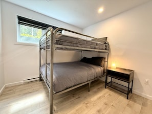 A bunk bed in a room with a window, a bedside table with a lamp, and wooden flooring. - Zénitude En Forêt Chalet – Spa & Precious Moments (Saint-Damien-de-Buckland)