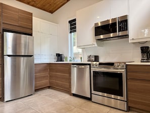 A modern kitchen with stainless steel appliances, wooden cabinets, and a window providing natural light.