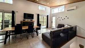 A modern interior with a dining area, a sofa, a TV, and a staircase. - Zénitude En Forêt Chalet – Spa & Precious Moments (Saint-Damien-de-Buckland)