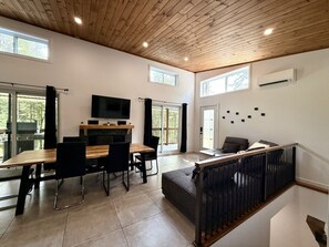 A modern interior with a dining area, a sofa, a TV, and a staircase. - Zénitude En Forêt Chalet – Spa & Precious Moments (Saint-Damien-de-Buckland)